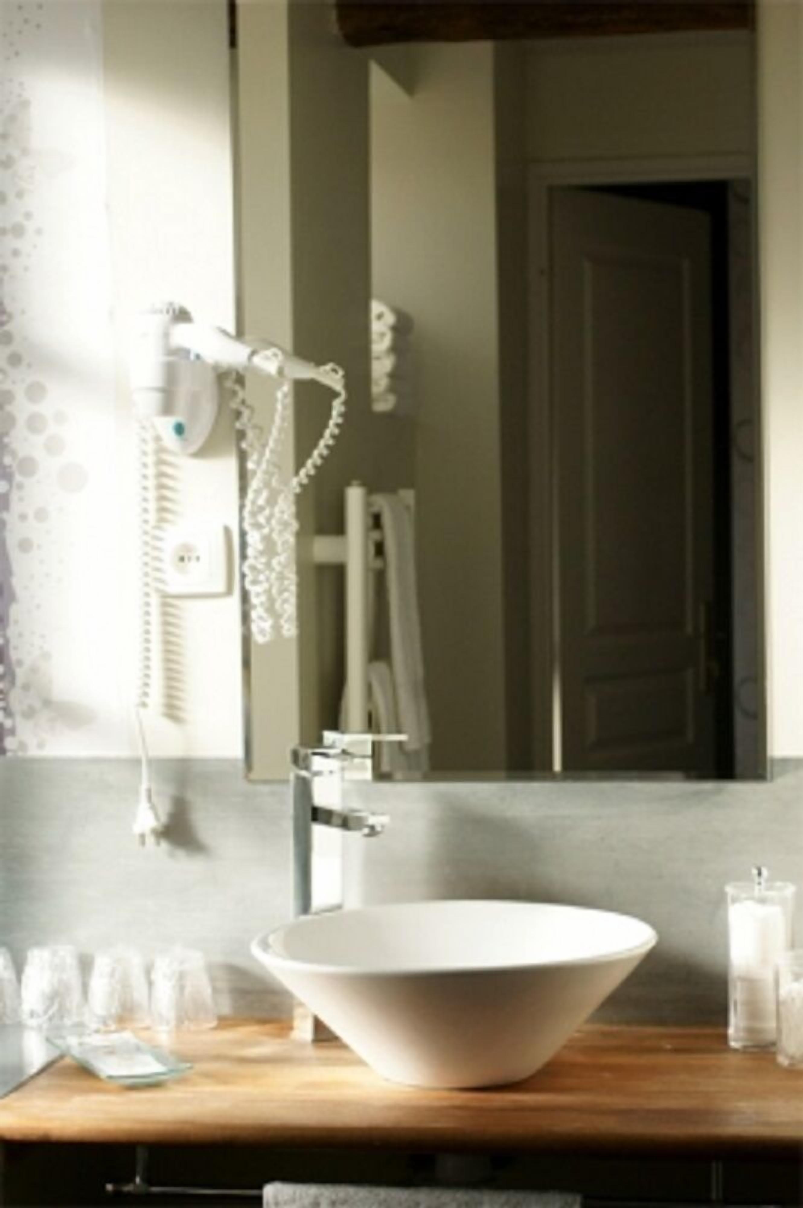 A bathroom with a large white sink, a mirror, a towel rack, and a hairdryer on the wall.