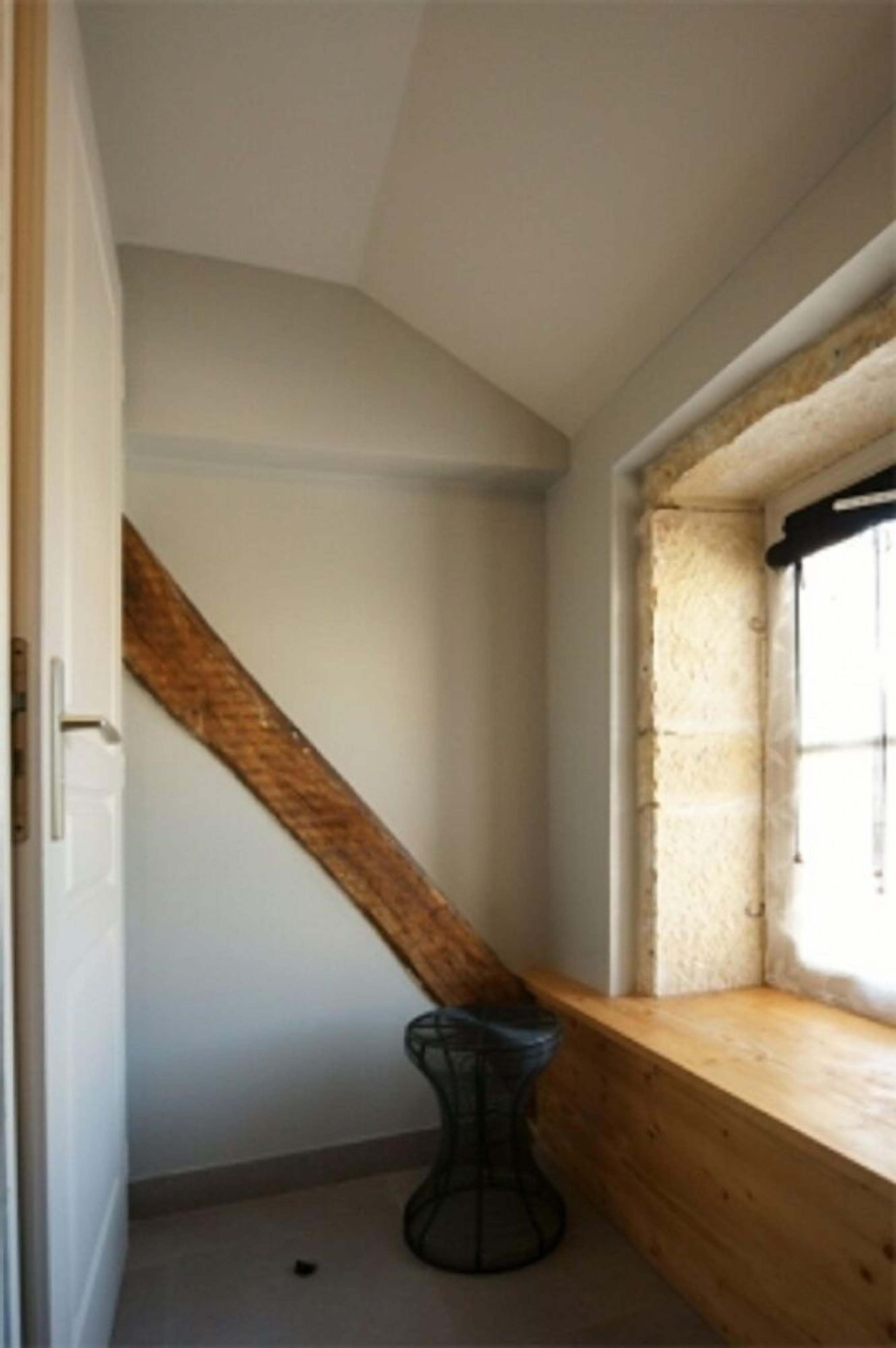 A room with a sloped ceiling, a wooden bench, a small stool, and a window with a view.