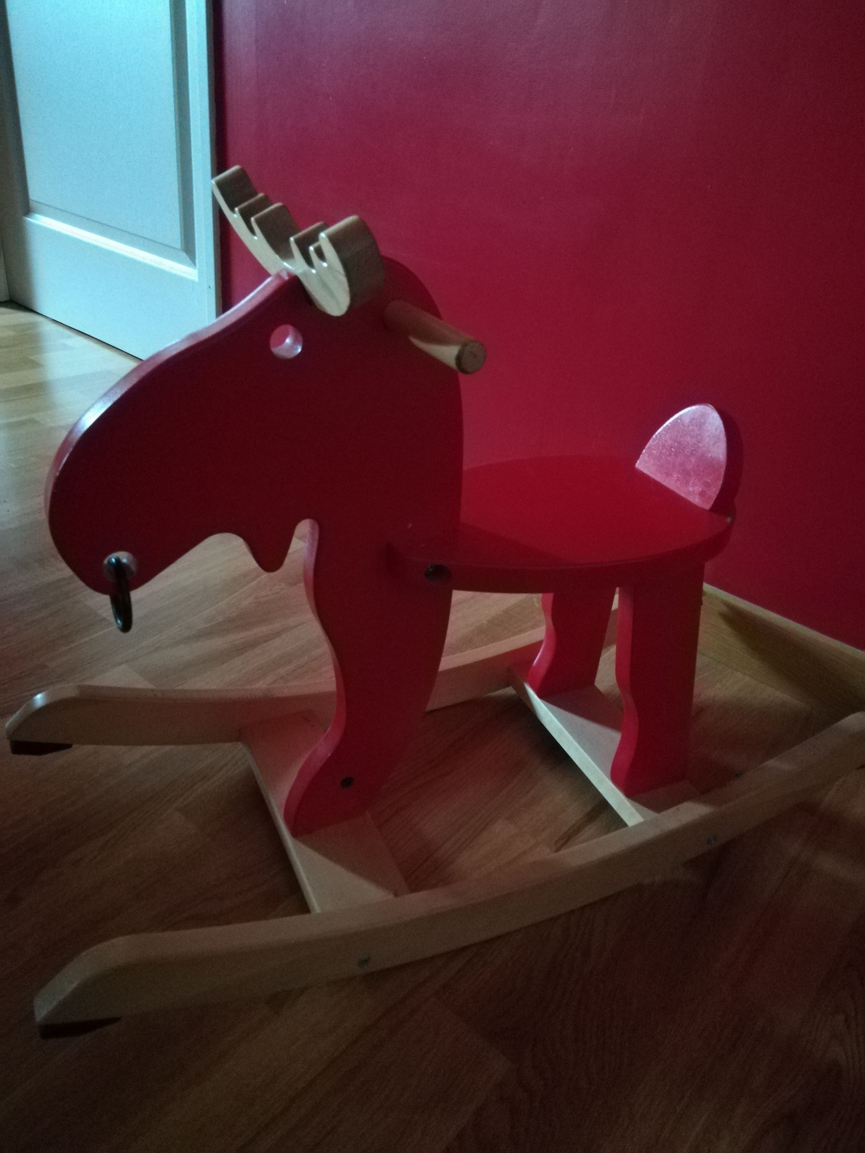 Un caballo balancín rojo en una habitación con suelo de madera y pared roja.