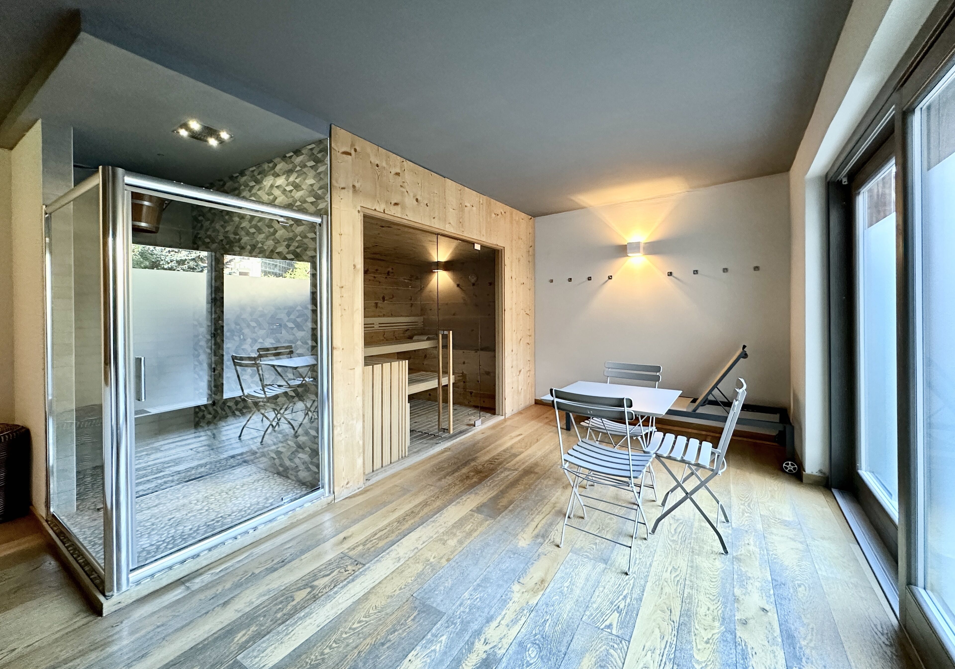 Un interior moderno con un ventanal de vidrio que da a un patio, una mesa de comedor con sillas y una lámpara fijada a la pared.