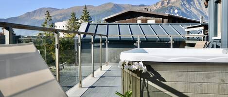 A rooftop terrace with a glass balustrade, a hot tub, and a potted plant.