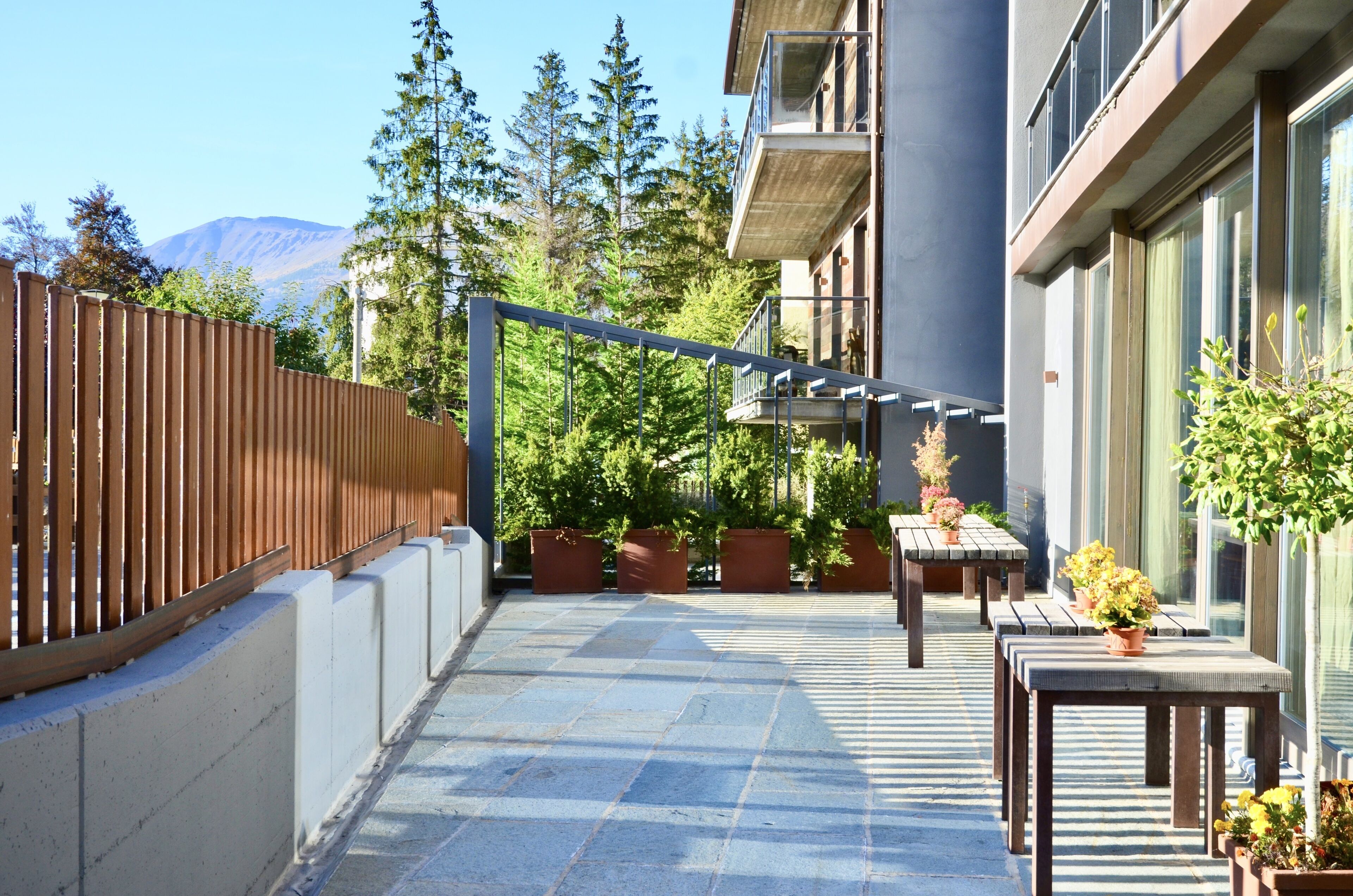 Un patio con cerco de madera, plantas en macetas y vista a la montaña.