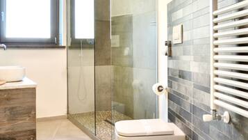 Un baño moderno con ducha de vidrio, un lavamanos grande y un inodoro.