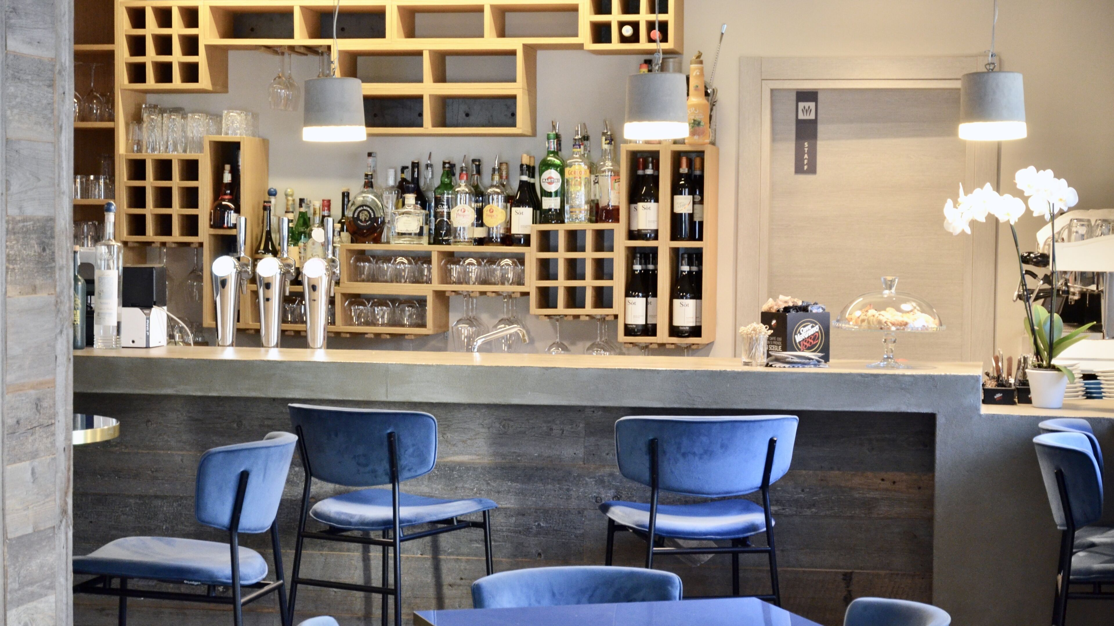 Zona de bar con estante de madera que exhibe diversas botellas, vasos y un letrero que dice 'STAFF'.