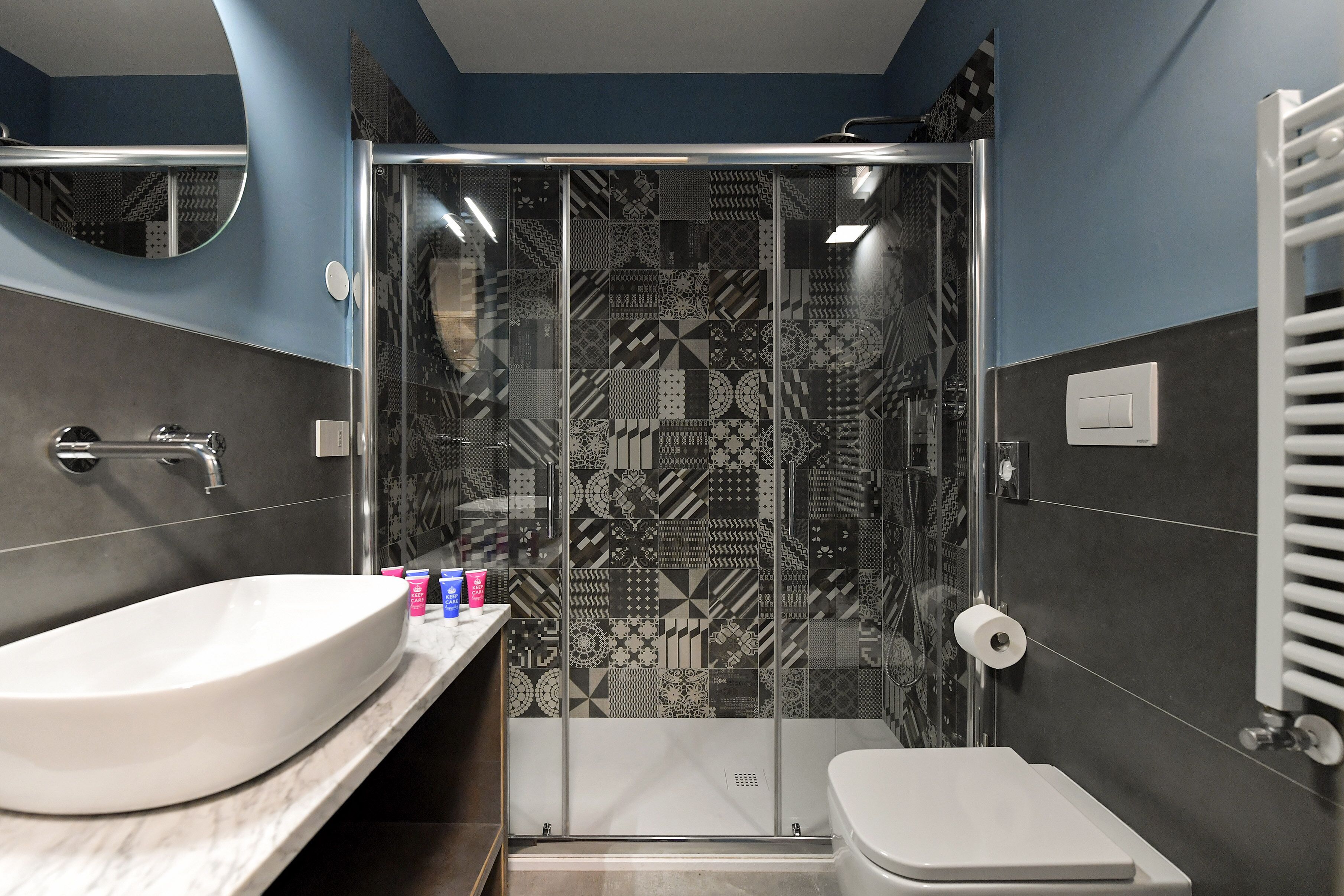 A modern bathroom with a large white sink, a shower enclosure with patterned tiles, and a toilet.