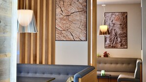 A modern interior with a wooden slat wall, a large tree ring artwork, a grey sofa, and a small table with a green candle. - Du Parc Hotel (Sauze d'Oulx)