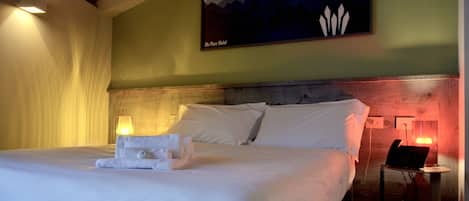 A hotel room with a bed, a nightstand, a lamp, and a painting on the wall.