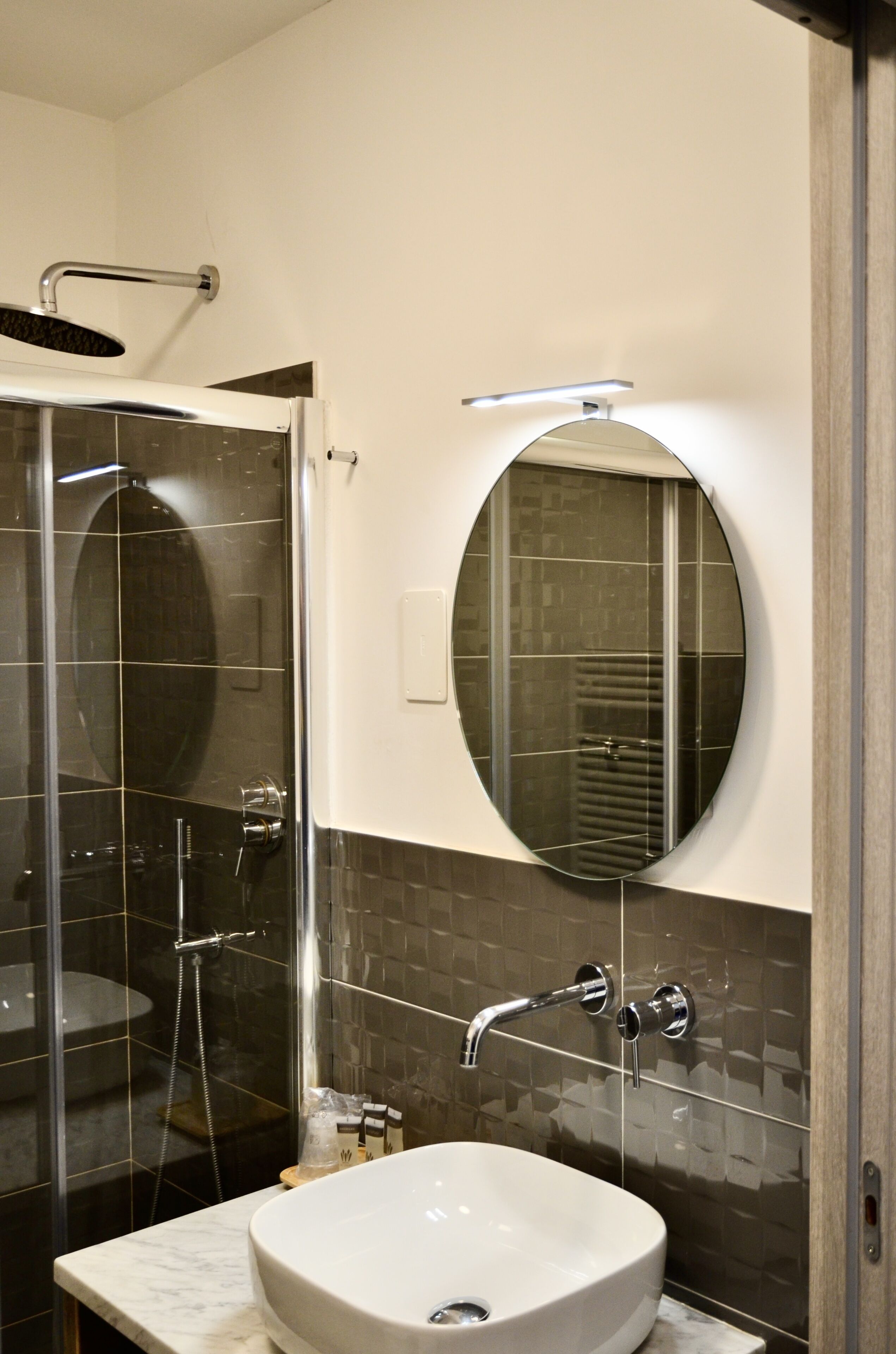 A modern bathroom with a glass-enclosed shower, a round mirror, and a marble sink.