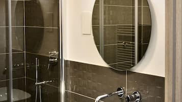 A modern bathroom with a glass-enclosed shower, a round mirror, and a marble sink.