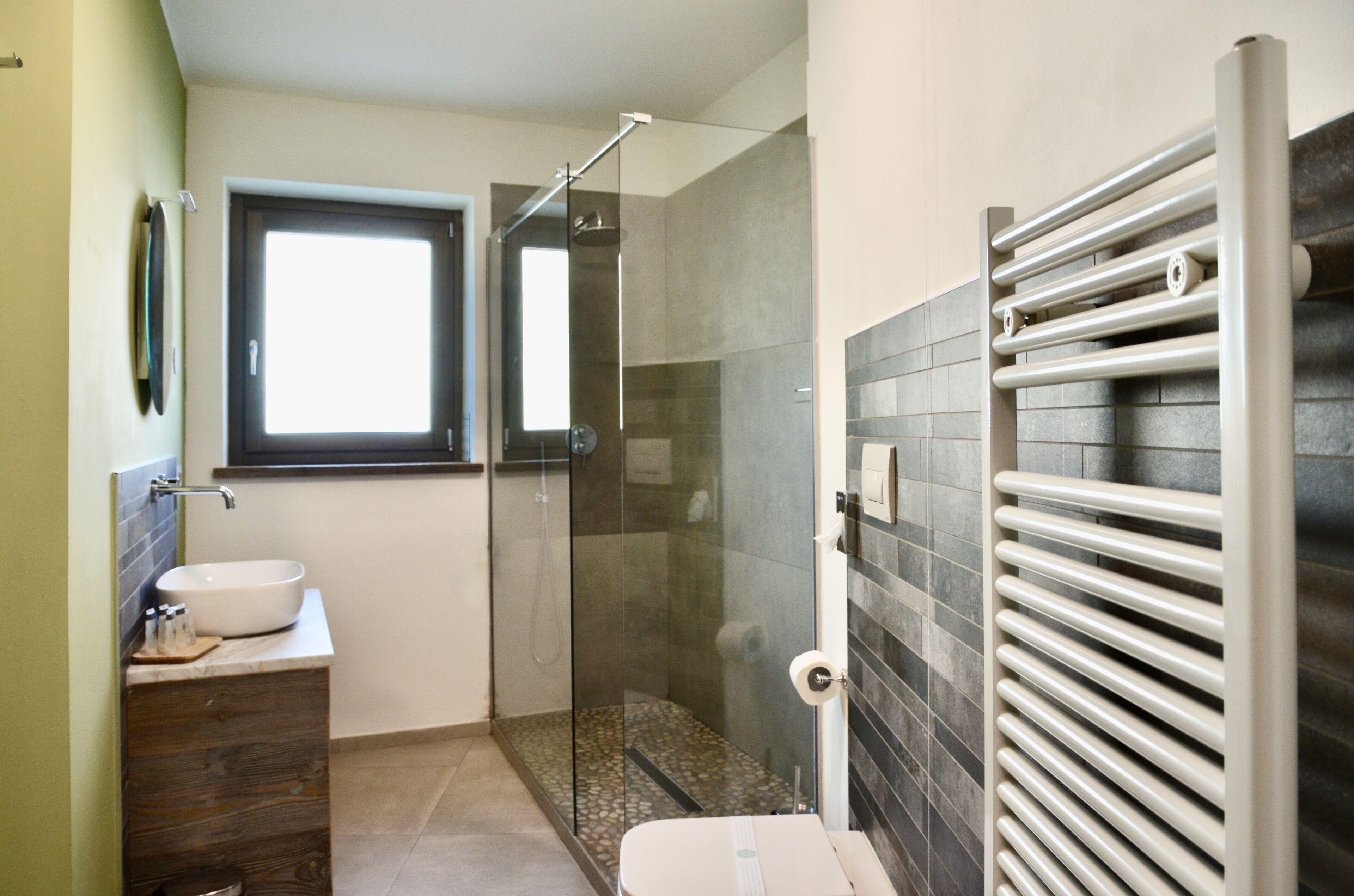 Un baño moderno con ducha envuelta en vidrio, un lavamanos con tocador de madera y un perchero para toallas.
