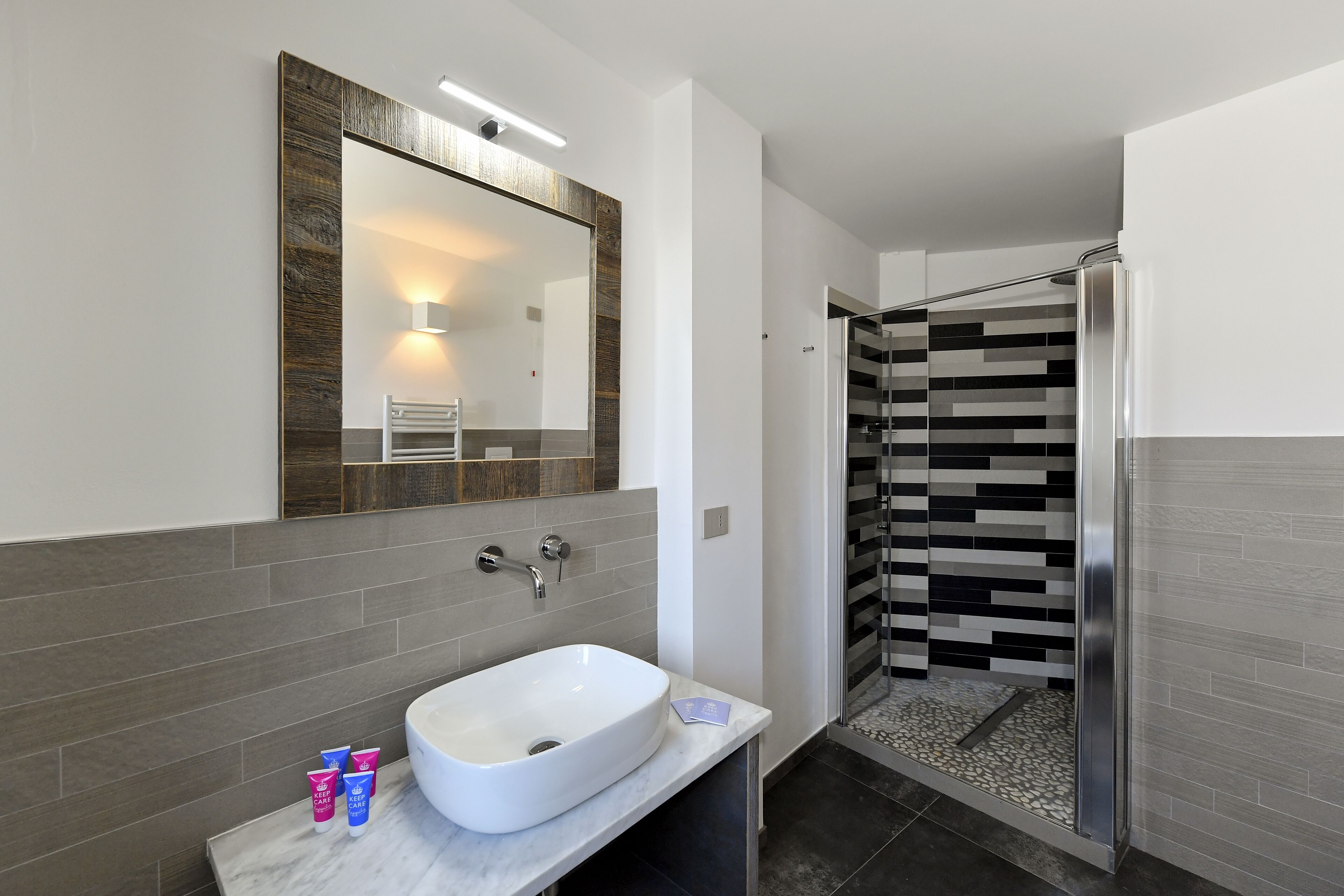 A modern bathroom with a large mirror, a white sink, and a shower area with a patterned tile wall.