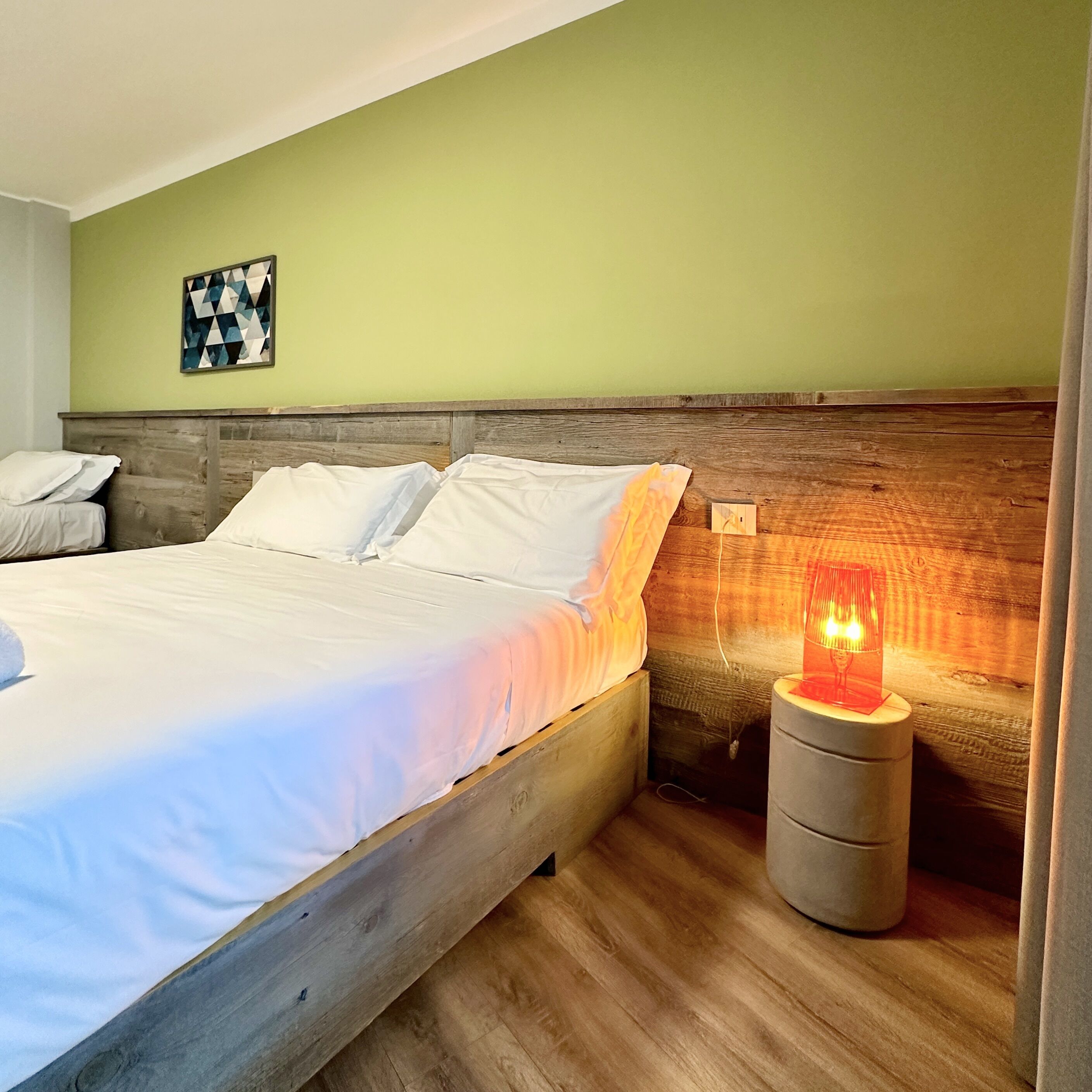 A neatly made bed with white linens, a wooden headboard, and a small bedside table with a red lamp.