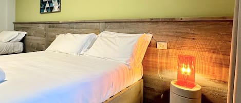 Una cama bien tendida con ropa blanca, un cabecero de madera y una mesita de noche con una lámpara roja.
