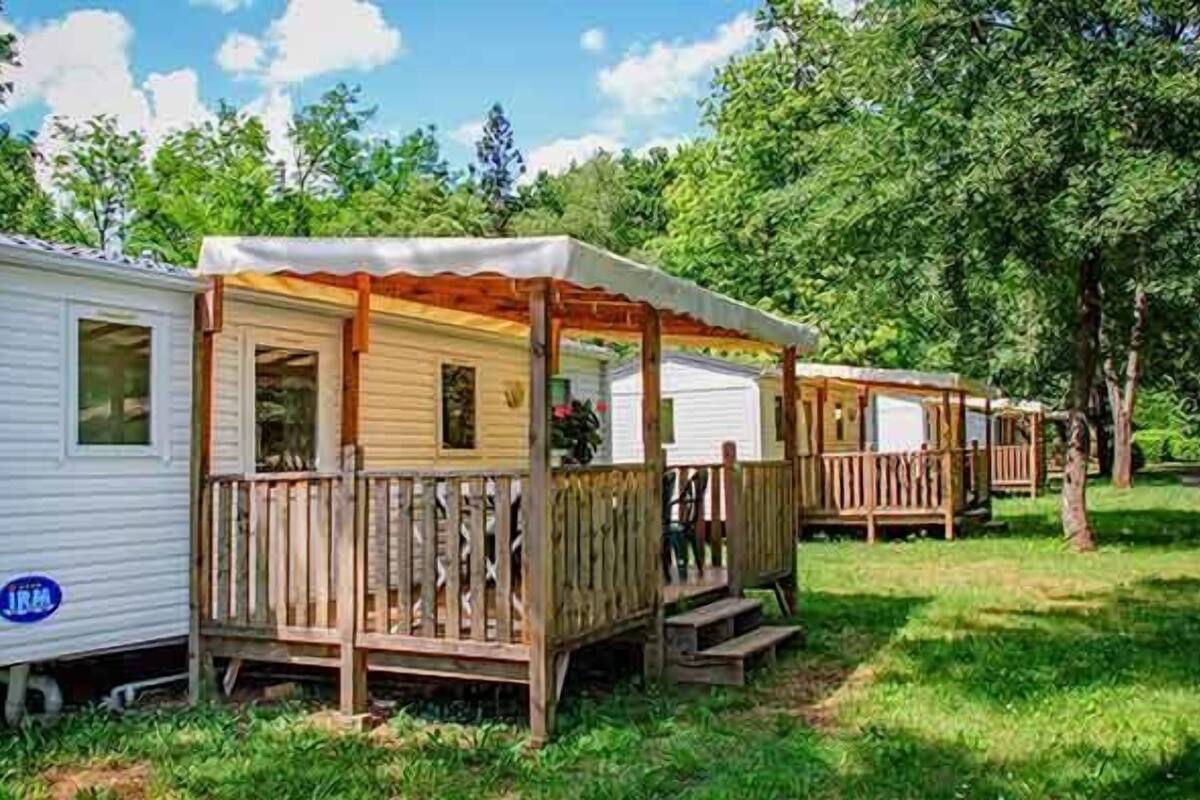A row of mobile homes with wooden decks and porches, surrounded by trees.