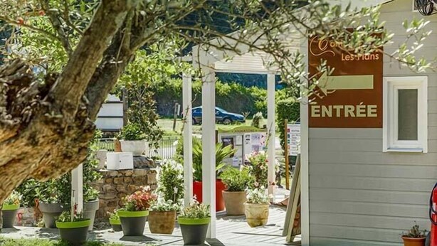 Un espacio al aire libre con plantas en macetas, una estructura de piedra y un letrero que dice 'ENTRÉE' indicando una entrada.
