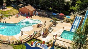 Una gran piscina al aire libre con tobogán, rodeada de sillas de descanso y un pequeño edificio.