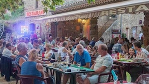 Un restaurante al aire libre concurrido, con paredes de piedra y un cartel que dice 'RESTAURANT'.