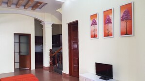 Ein geräumiger Wohnbereich mit Flachbildfernseher auf einem weißen Schrank, einer roten Bank und drei gerahmten Bildern an der Wand.