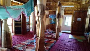 Ein traditionell eingerichteter Holzraum mit vier Betten, jedes mit farbenfroher Bettdecke und Baldachin.