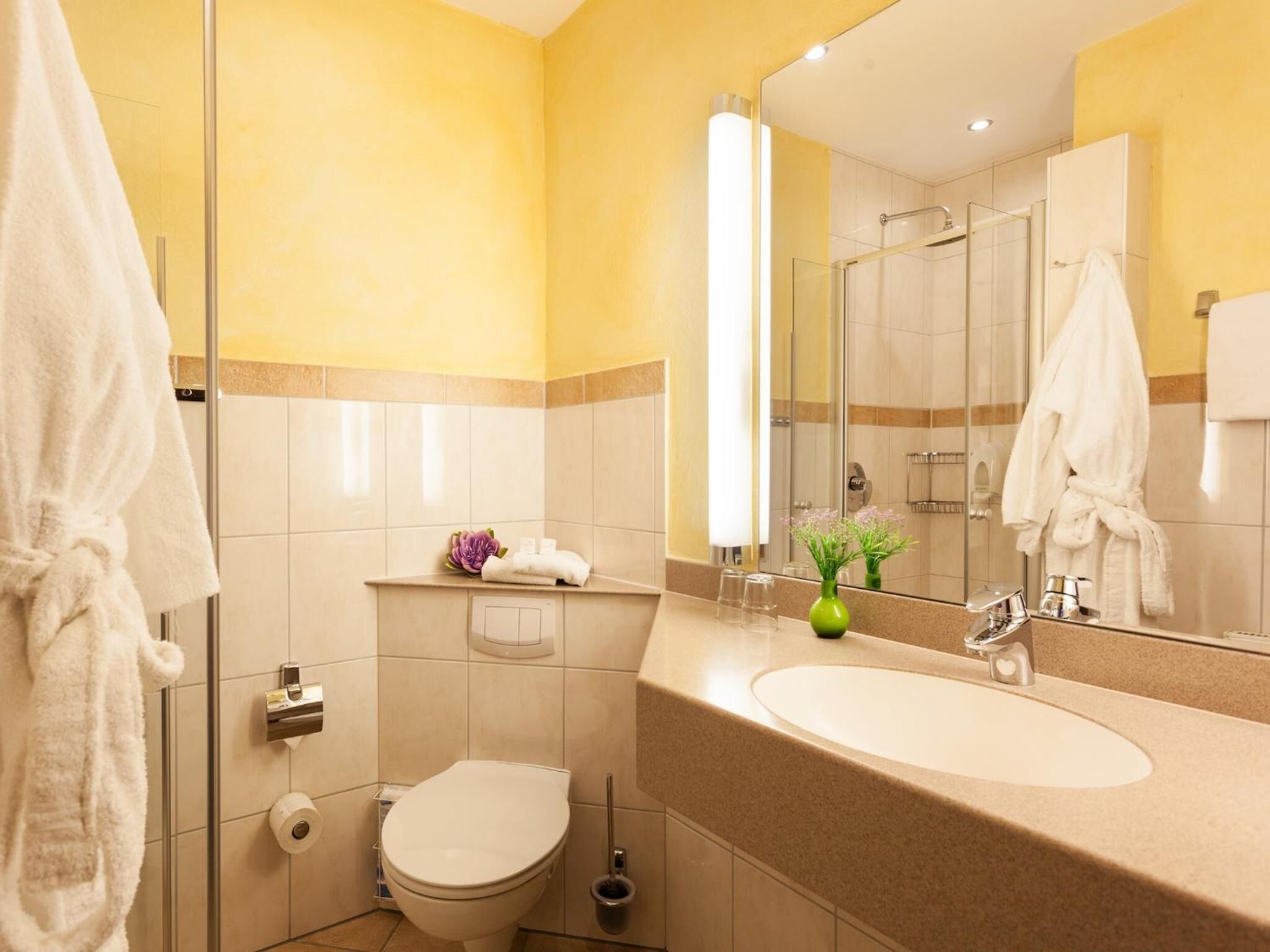 Ein Badezimmer mit Toilette, Waschbecken, Spiegel und Duschkabine aus Glas.