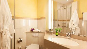 Ein Badezimmer mit Toilette, Waschbecken, Spiegel und Duschkabine aus Glas.