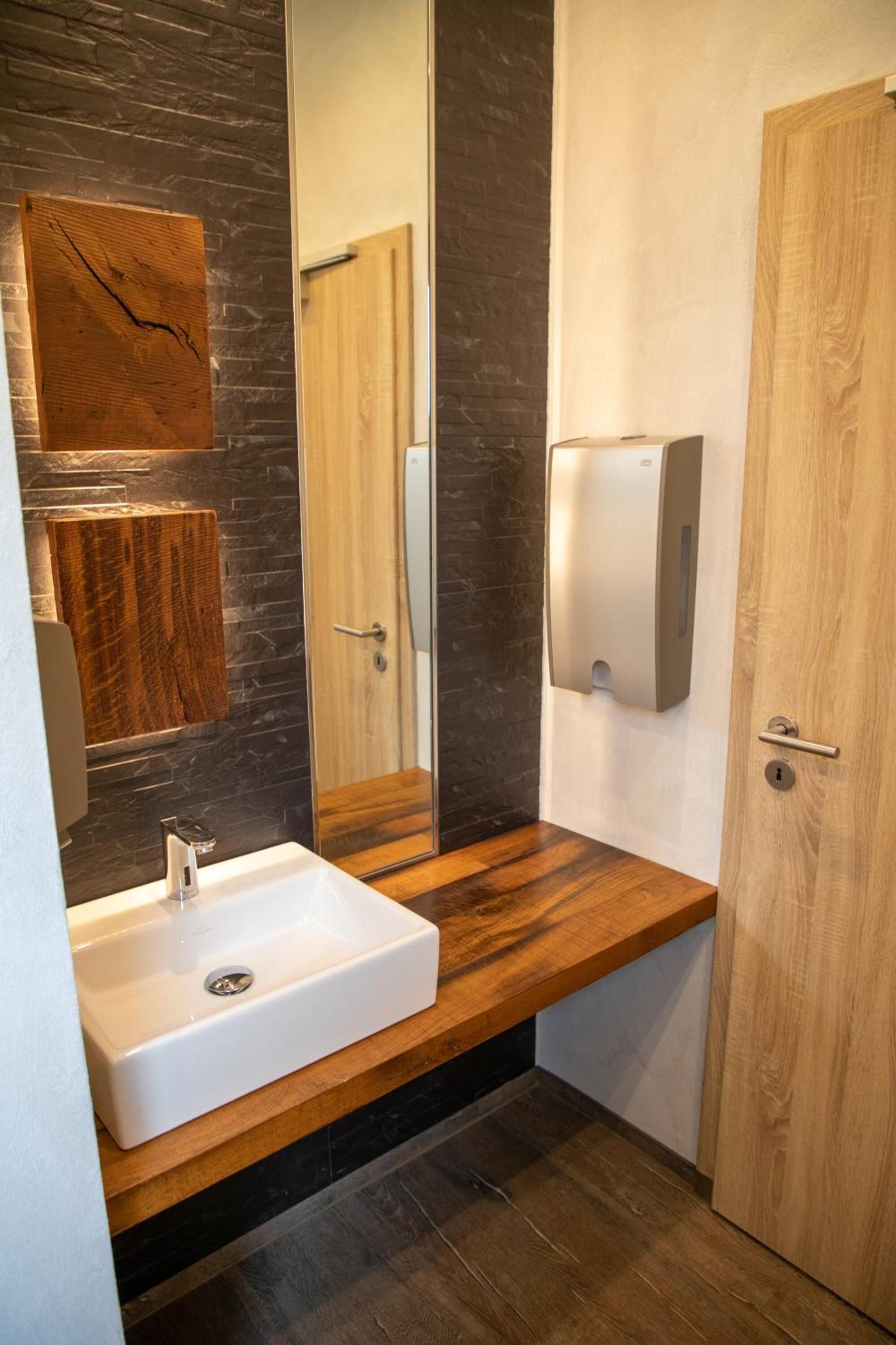 Un bagno moderno con un mobile bagno in legno, un grande specchio, un lavandino bianco e un asciugamani ad aria.