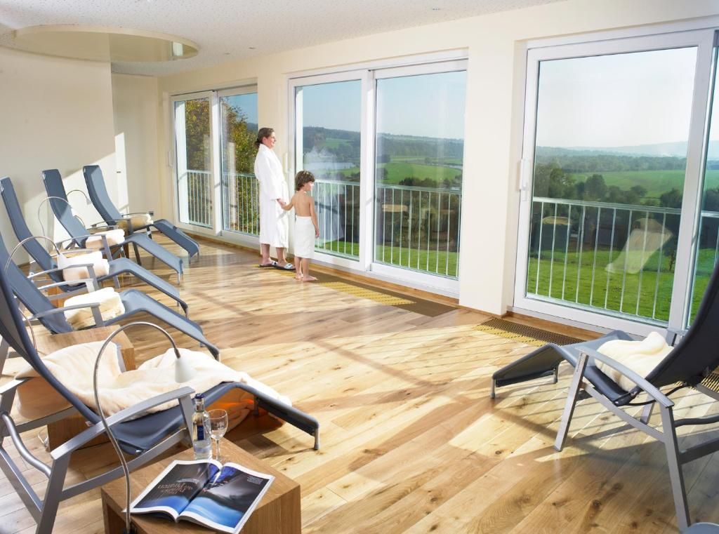 A room with a wooden floor, a balcony with a glass railing, and a view of the countryside.