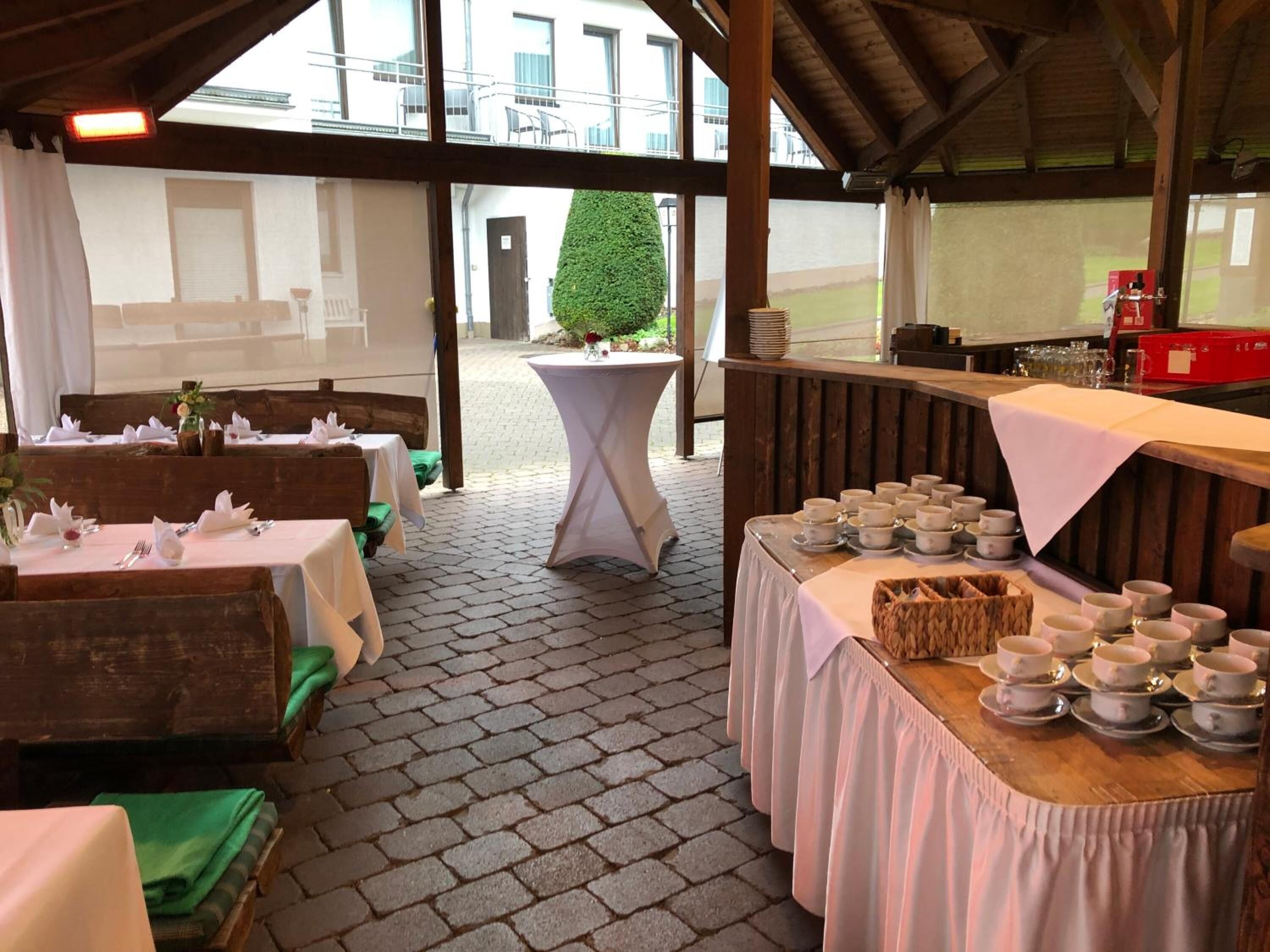 An outdoor dining area with tables set for a meal, a buffet table with bowls, and a view of a building in the background.