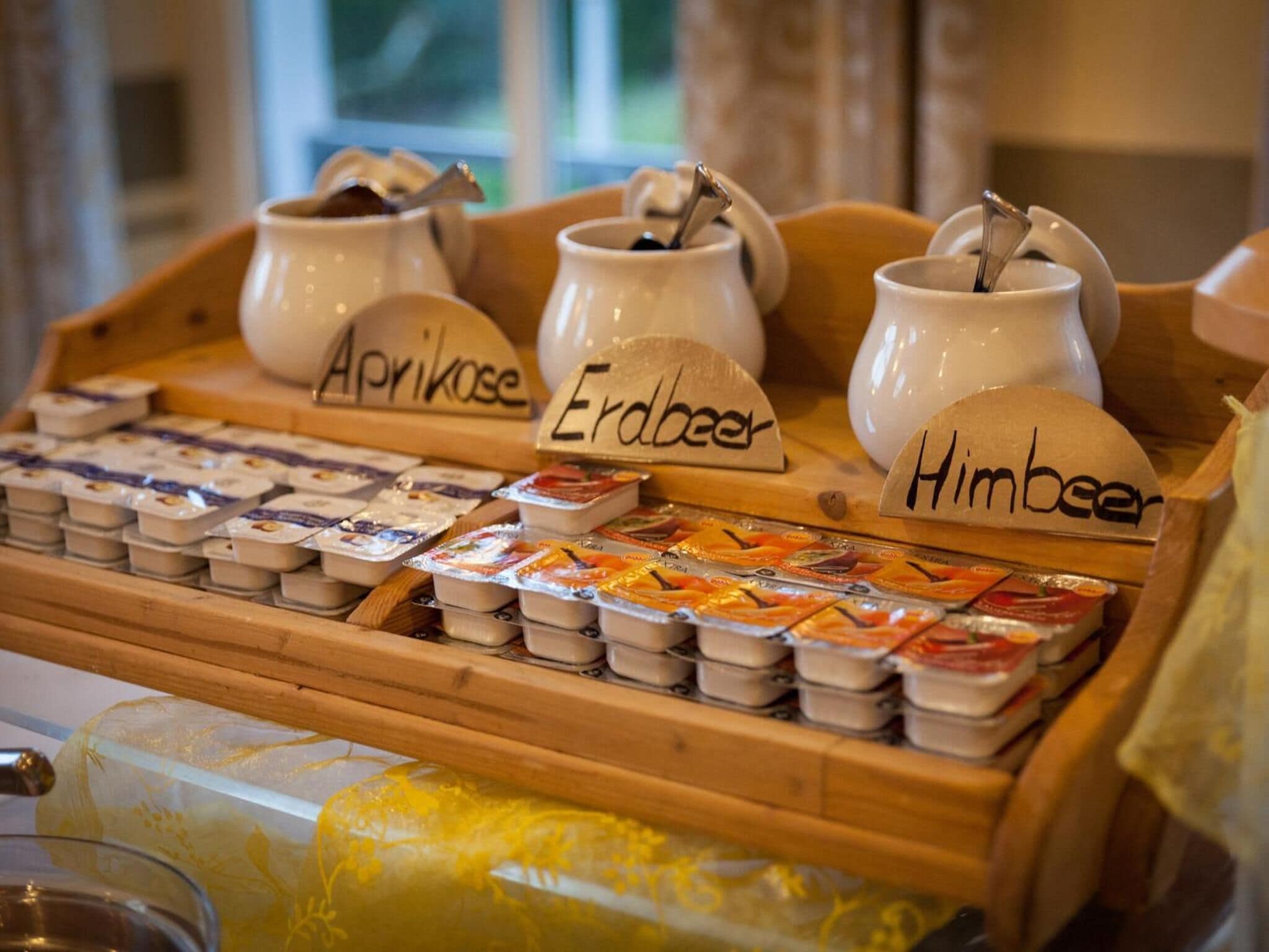 A selection of cheeses and yogurts on a wooden display with labels for Aprikose, Erodbeer, and Himbeers.