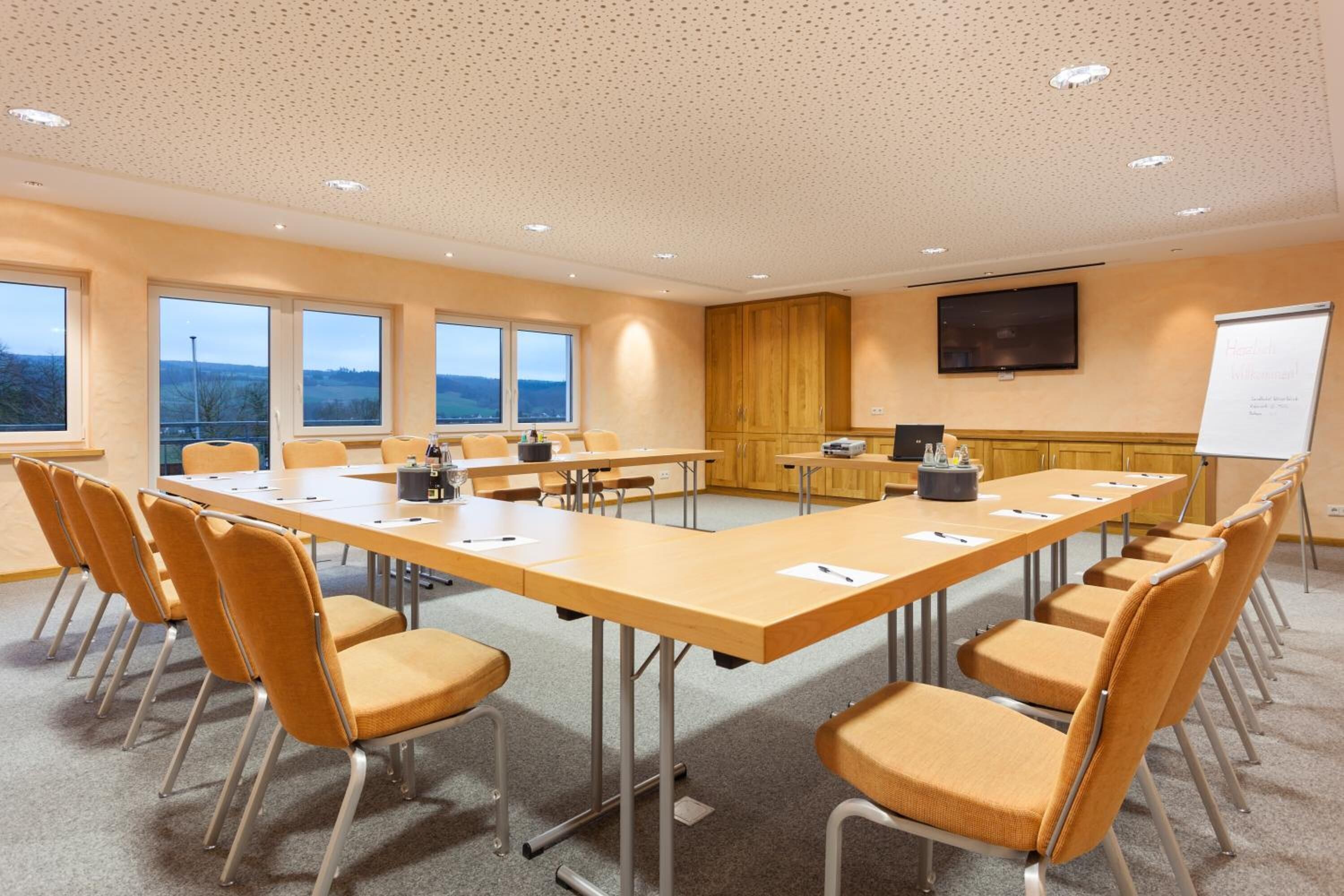 Een vergaderzaal met een lange tafel, stoelen, een whiteboard en een televisiescherm.