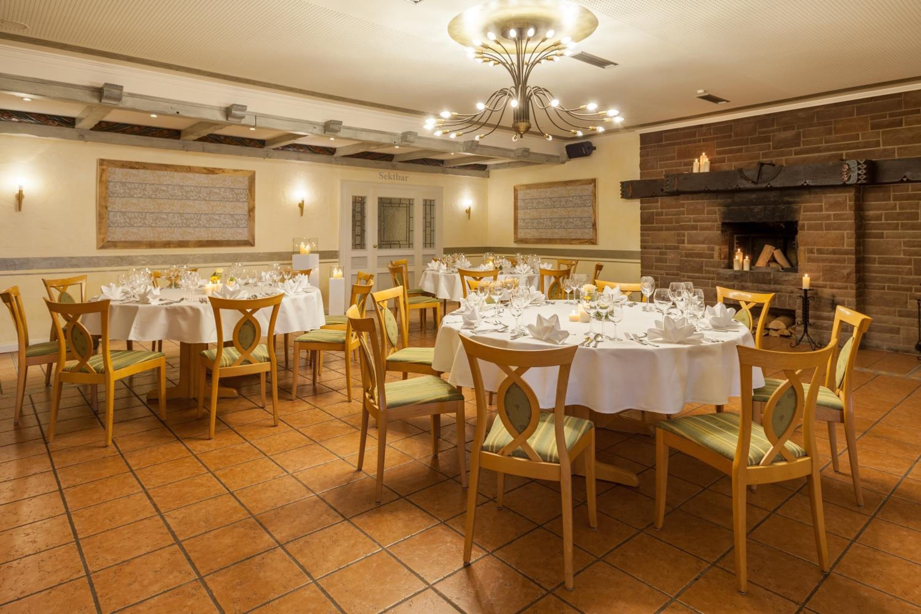 A dining area with round tables set for a meal, wooden chairs, and a brick fireplace.