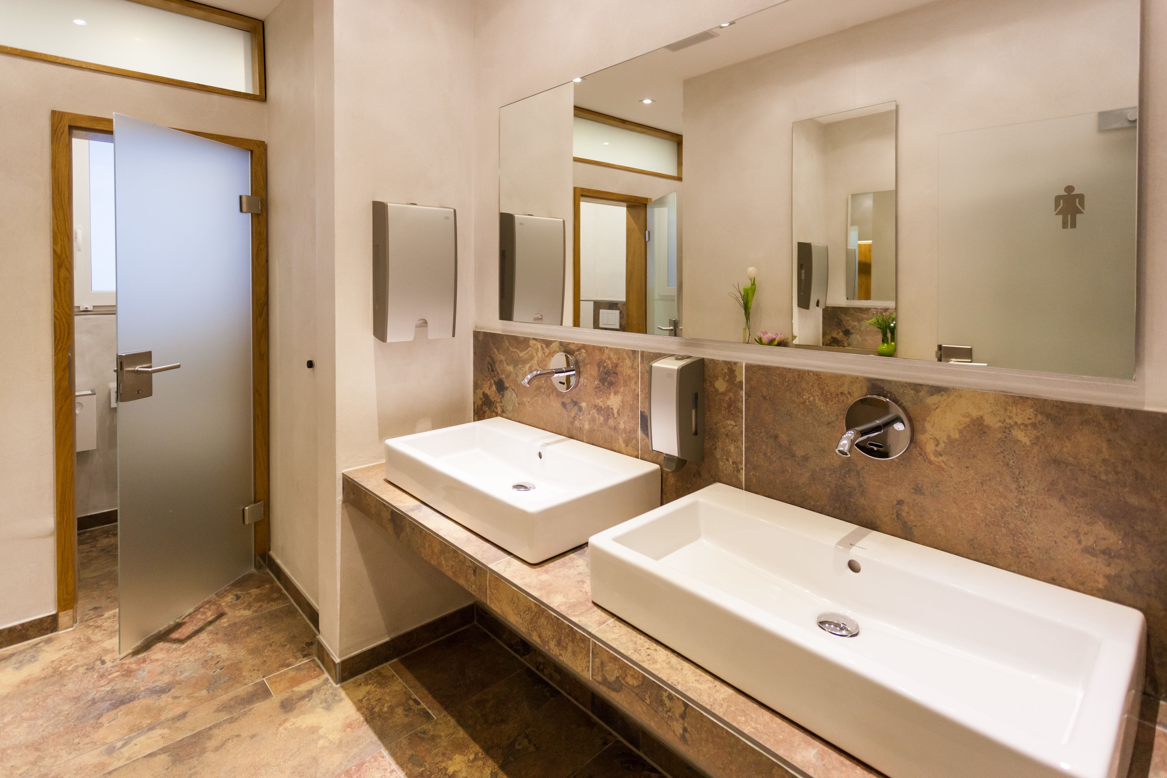 A modern bathroom with two sinks, a large mirror, and a door leading to another room.
