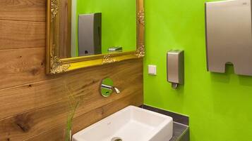 A bathroom with a wooden vanity, a white sink, a green wall, a gold-framed mirror, and a soap dispenser.