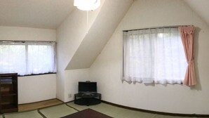 Een kamer met een schuine balklaag, een bankje, een tv-meubel en een raam met gordijn.