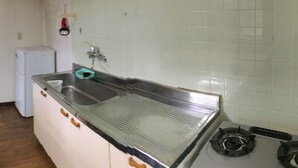 Een keuken met witte kastjes, een roestvrijstalen spoelbak, een gasfornuis en een kleine koelkast.