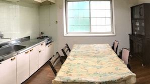 Een keuken met een eettafel, stoelen, kastjes, een raam en een spoelbak.