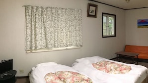 Een hotelkamer met twee bedden, een raam met bloemen gordijnen, een oranje bank, een klein tafeltje en een schilderij aan de muur.