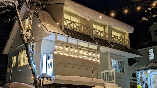 Een huis met twee verdiepingen, een met sneeuw bedekte dak en een balkon met lichtjes.
