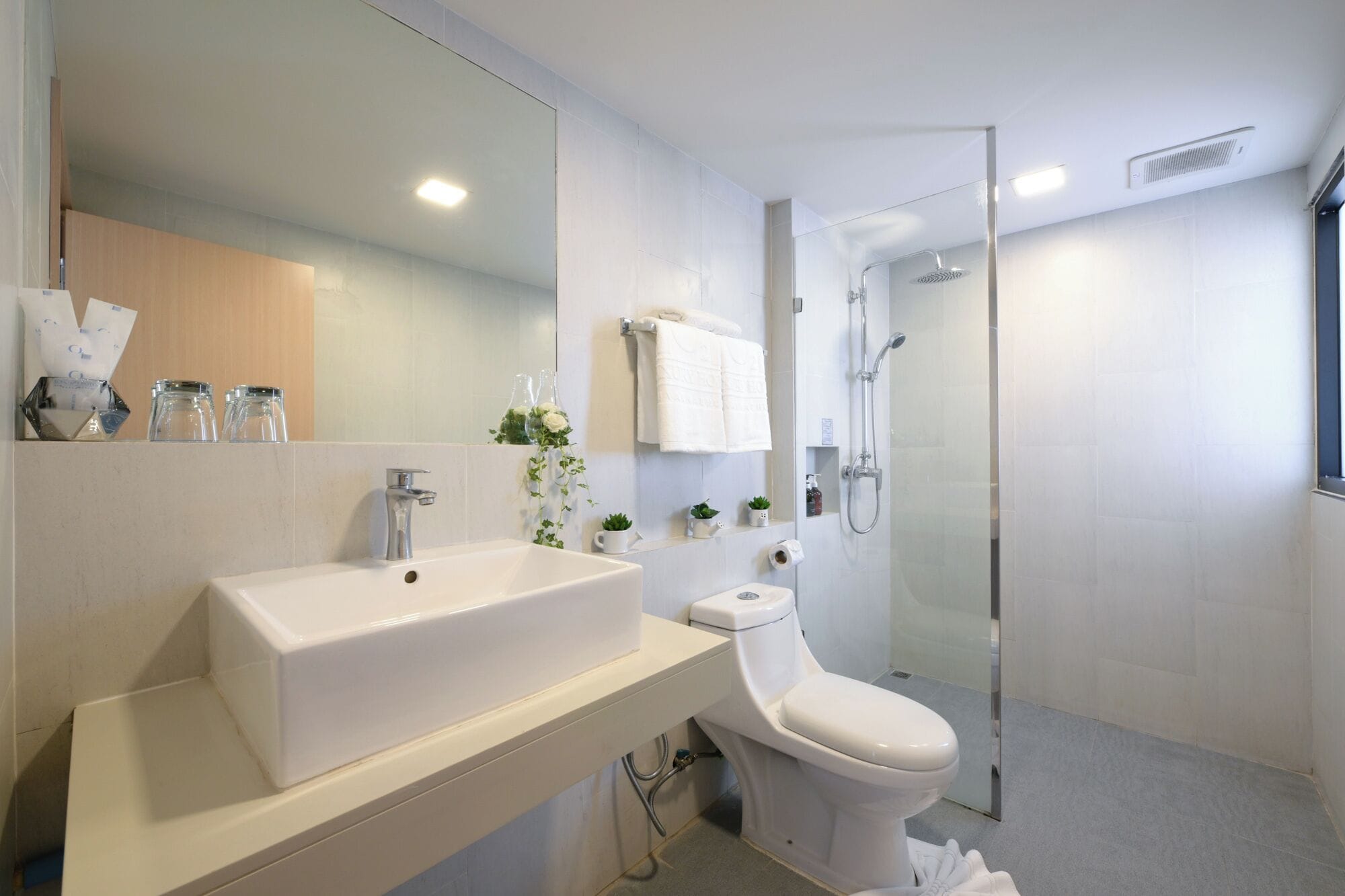 Ein modernes Badezimmer mit großem Spiegel, weißem Waschbecken, Toilette und Duschkabine.