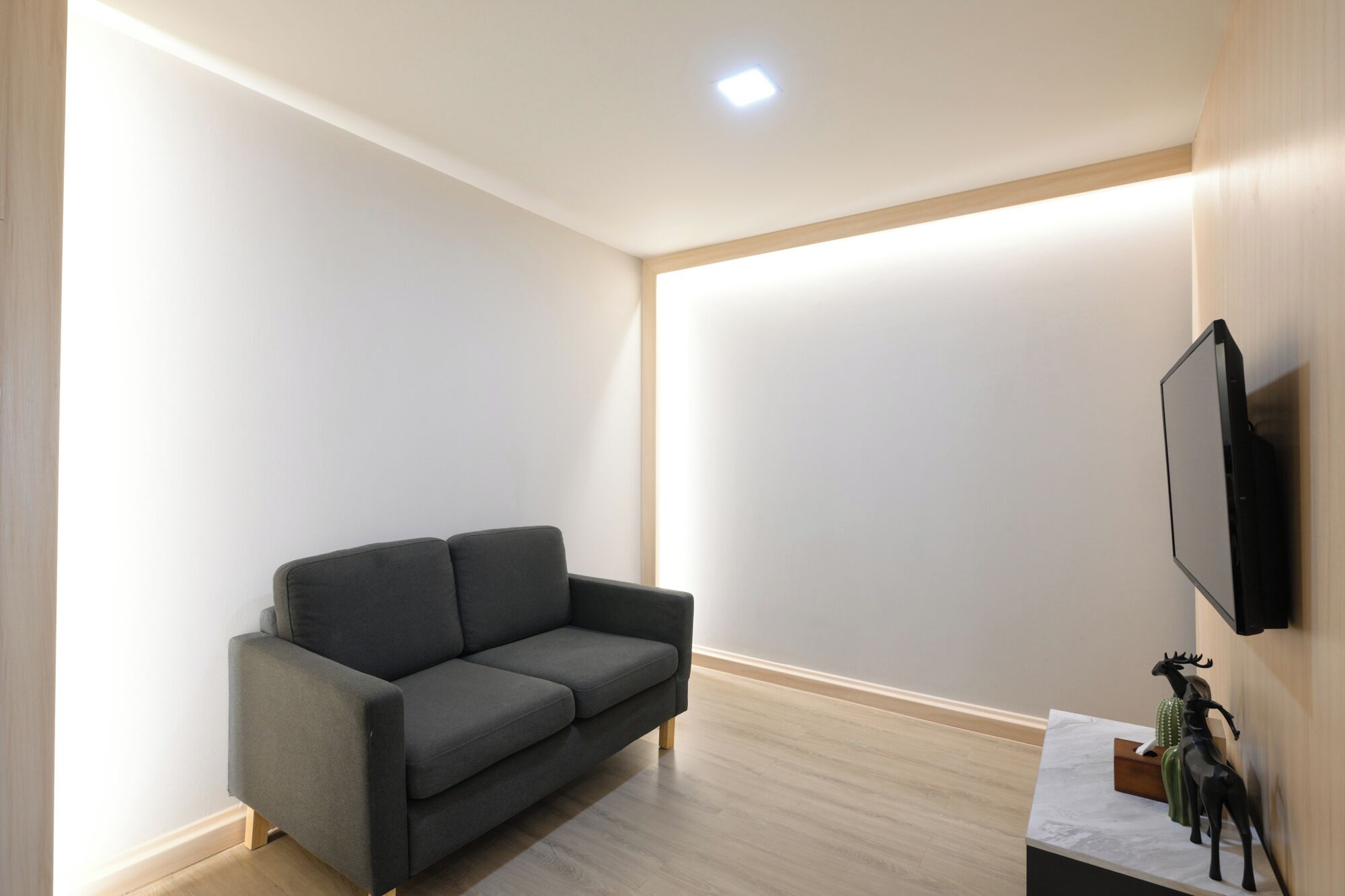 Un salón moderno con un sofá gris, un televisor de pantalla plana montado en la pared y una mesita con objetos decorativos.