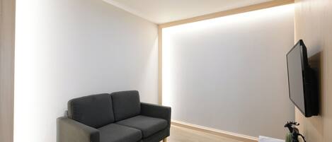 A modern living room with a grey sofa, a flat-screen TV mounted on the wall, and a small table with decorative items.