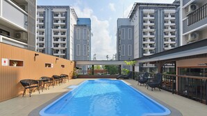 A swimming pool with surrounding lounge chairs and a view of adjacent buildings.