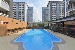 A swimming pool with surrounding lounge chairs and a view of adjacent buildings.