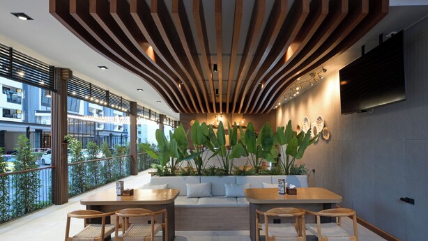 A modern outdoor seating area with wooden furniture, a large plant, and a TV mounted on the wall.