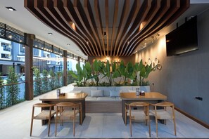 A modern outdoor seating area with wooden furniture, a large plant, and a TV mounted on the wall.