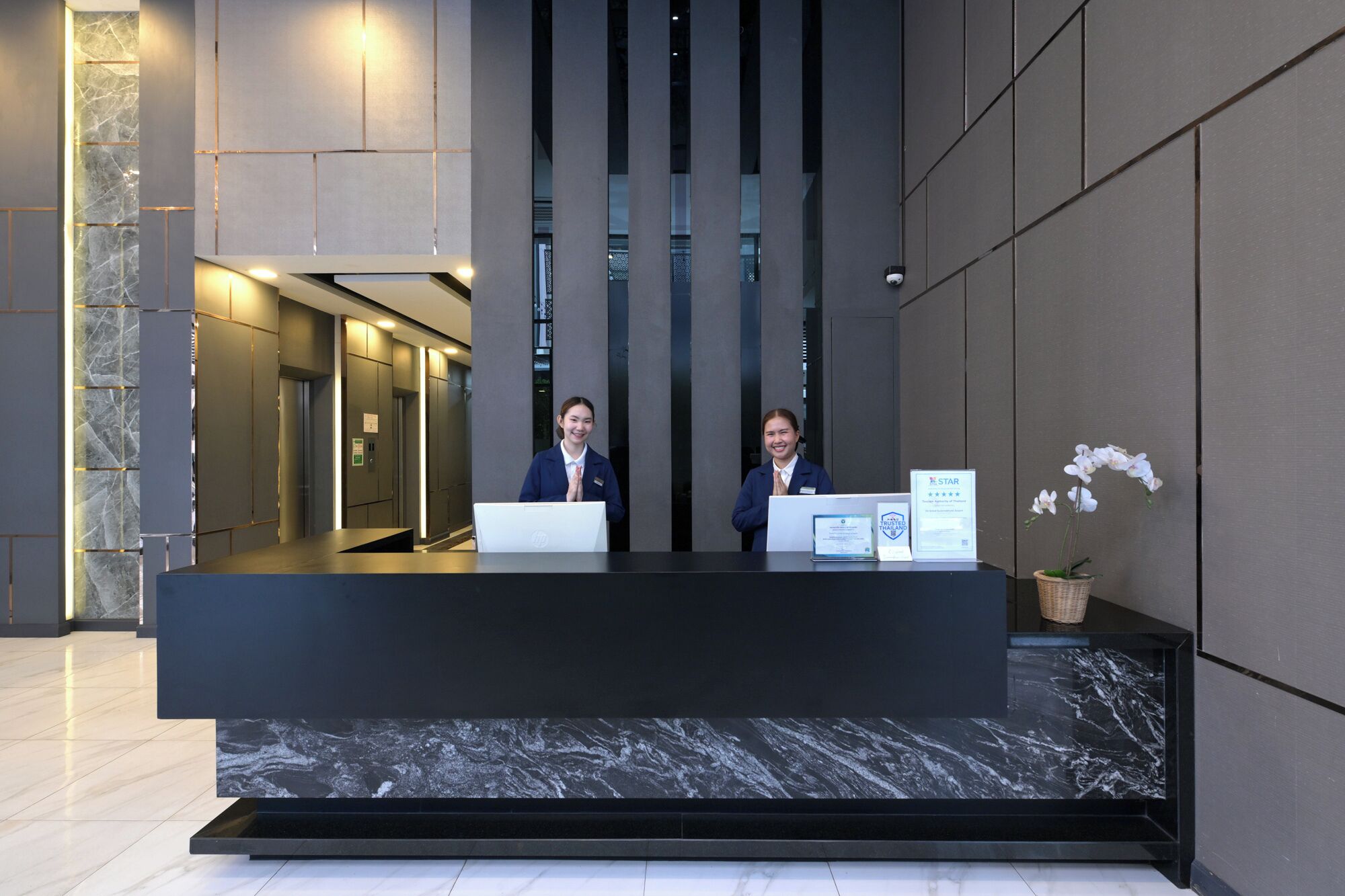 A reception desk with two staff members, a marble floor, and a wall with vertical panels.