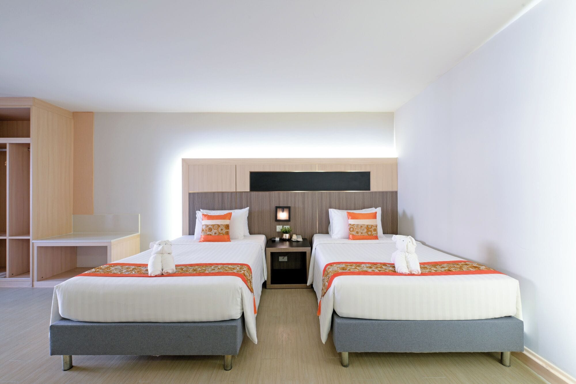 A hotel room with two beds, a desk, a wardrobe, and a flat-screen TV.