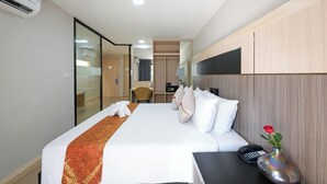 A hotel room with a bed, a desk, a phone, and a vase with a rose.