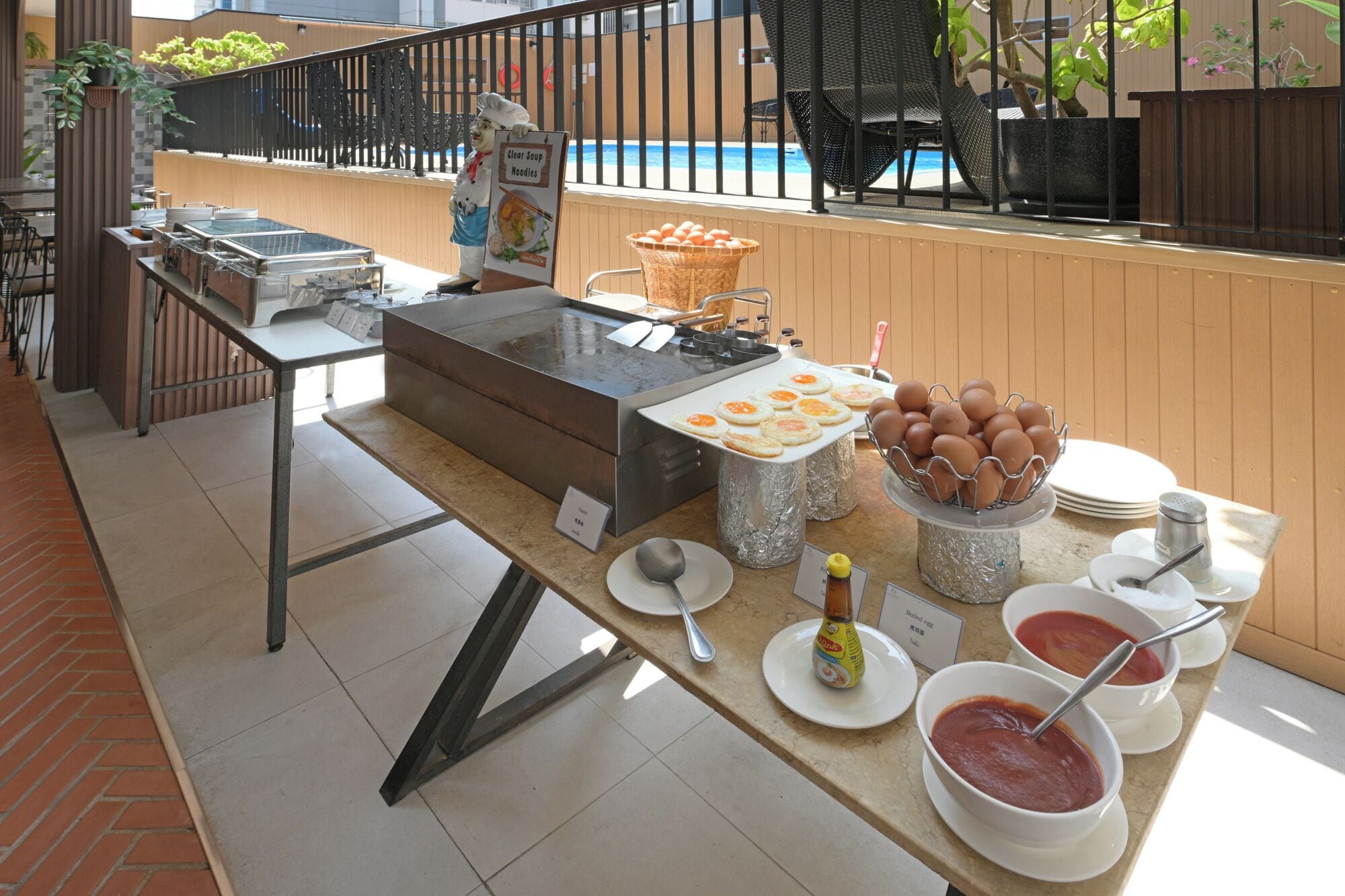 Un buffet de petit-déjeuner avec un panneau indiquant les nouilles en bouillon, un panier d’œufs et des bols de soupe.