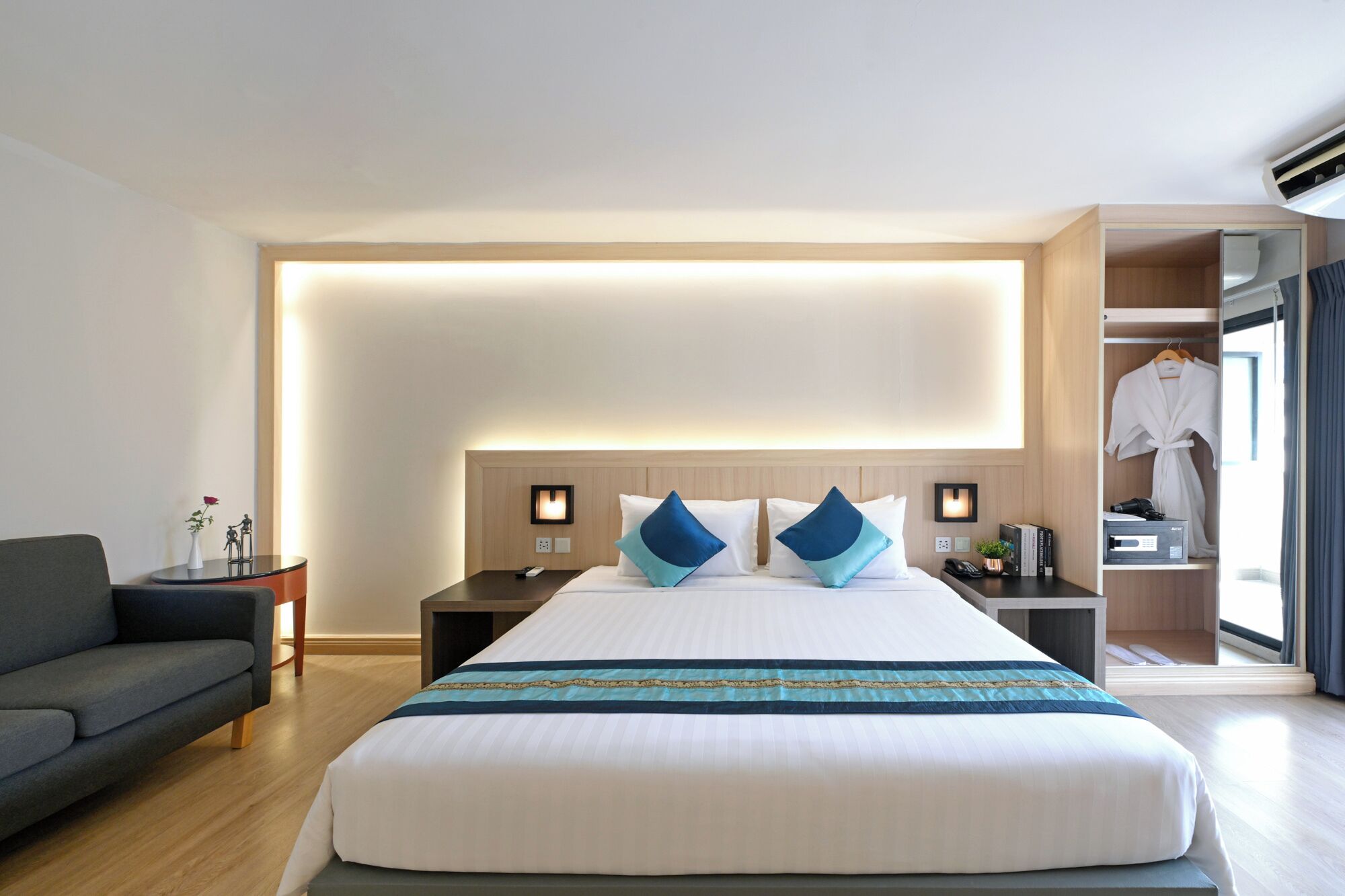 A hotel room with a large bed, bedside tables, a nightstand, a sofa, a wardrobe, and a mirror.